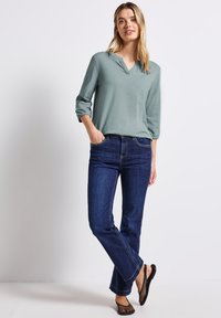 Jasnozielona koszula z długim rękawem i dekoltem w szpic; zestawiona z ciemnoniebieskimi dzwonami i czarnymi płaskimi butami z siateczki. Miękka tkanina, luźny krój.