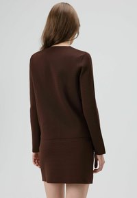 Bruin tweedelig outfit met een longsleeve top met een gestructureerde afwerking en een bijpassende aansluitende rok, gezien vanaf de achterkant.