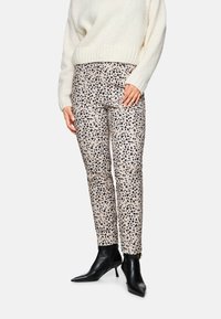 Beige Tiermuster-Hose mit schwarzen Flecken, figurbetontes Design, kombiniert mit einem cremefarbenen Strickpullover und schwarzen, spitzen Knöchelstiefeln.