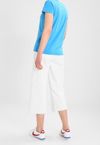 Modrá krátkosrstvá bavlněná tričko v kombinaci s bílými širokými třičtvrtečními kalhotami a bílými teniskami s červenými a modrými akcenty.