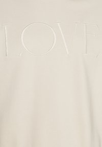 Sudadera de color crema con una textura suave que presenta la palabra "LOVE" en letras elevadas y cosidas en la parte frontal.