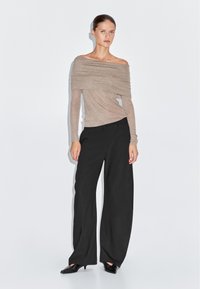 Beiges, schulterfreies Oberteil aus leichtem Stoff, kombiniert mit hochgeschnittenen schwarzen weiten Hosen und spitzen schwarzen Ballerinas.