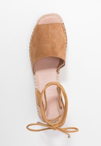 Hnědé semišové espadrilky s otevřenou špičkou, tkaným jutovým obvodem a hnědými šňůrkami. Hladký růžový vnitřek s kulatým tvarem.