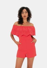 Tuta rossa scollata con bordi scallop in pizzo, di lunghezza corta, con tasche frontali e texture del tessuto liscia.