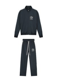 Donkerblauw trainingspak met witte accenten, bestaande uit een ritsjack en broek met koordjes, gemaakt van een gladde, lichte stof.