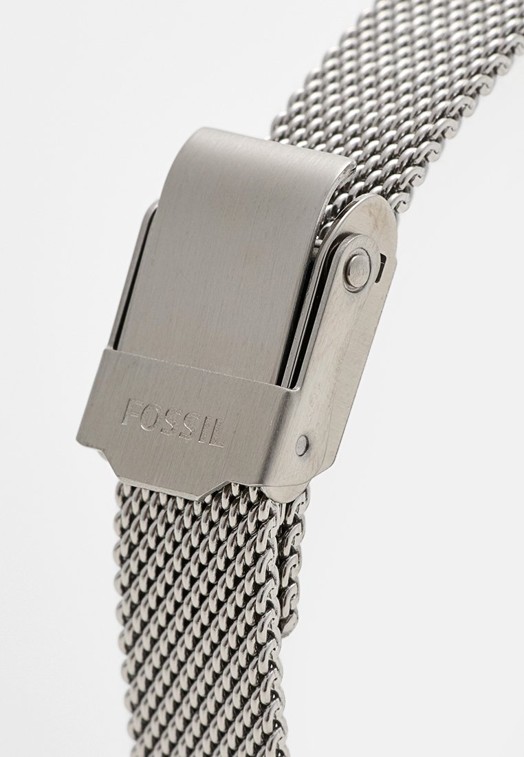 Cinturino in maglia d'acciaio inossidabile con chiusura in argento lucidato incisa con "Fossil". Il cinturino presenta una texture flessibile e intrecciata.