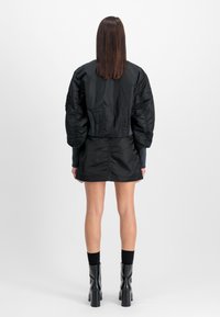 Czarna kurtka bomberka z puszystymi rękawami, połączona z czarną mini spódnicą, obie wykonane z gładkiego, błyszczącego materiału. Noszona z czarnymi kozaczkami na wysokim obcasie do kolan.