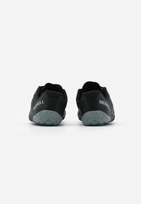 Un paio di scarpe slip-on nere Merrell con suole grigie texture, viste da dietro su uno sfondo bianco.