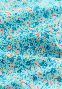 Tissu bleu clair avec un motif floral dense composé de petites fleurs dans des nuances de bleu, rose, jaune et vert, montrant de légers plis et une texture.