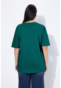 T-shirt in cotone verde con maniche corte, scollatura rotonda e vestibilità relaxed. Tessuto morbido con design semplice, indossato con jeans blu.