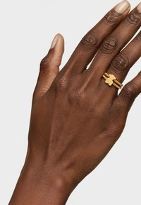 Gold-tone ring featuring a textured band and a unique bear-shaped accent. Worn on a dark skin tone hand with well-groomed nails.