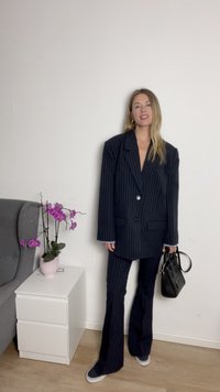 Navystriped dressjakke med dobbeltknapp, sammen med vide bukser, kombinert med en svart håndveske og lave sneakers. Innendørs setting.