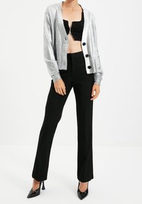 Srebrny kardigan o prążkowanej fakturze, zapinany na guziki, z czarnym krótkim topem. Czarne, dopasowane spodnie o prostych nogawkach, zestawione z czarnymi szpilkami o spiczastym nosku.