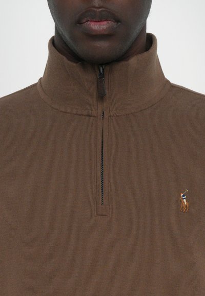 Bruine geribbelde pullover met een kwart rits en een klein geborduurd logo van een polo speler op de linkerkant van de borst.