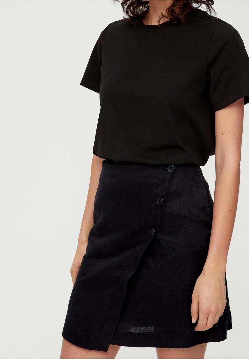 T-shirt en coton noir à manches courtes associé à une jupe en lin foncé taille haute avec une fermeture à bouton sur le côté et un design légèrement drapé.