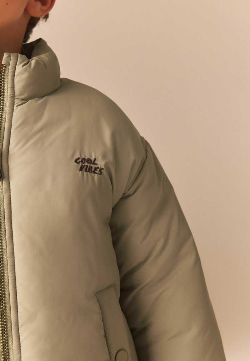 Ljusgrön pufferjacka med hög krage, dragkedjestängning och broderad "Cool Vibes"-logotyp på bröstet. Slät, vadderad textur.
