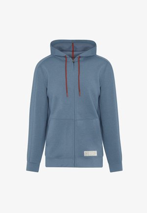 KAPPET HEHET I LYS BLÅTT STOFF MED RØDE SNORE. HAR LOMME FORAN OG EN MERKING PÅ NEDKANTEN, GLATT TEKSTUR, OG LØS PASSFORM.