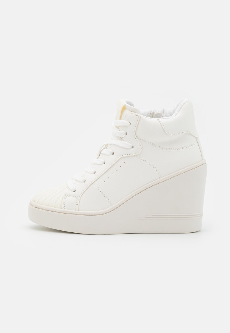 Sneaker compensée blanche montante avec lacets sur le devant, col de cheville rembourré et bout texturé, vue de côté externe sur fond blanc.