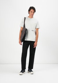 Lys grå bomulds t-shirt med korte ærmer og diskret branding, parret med sorte lige ben bukser og navy sneakers. Grå skuldertaske.