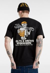 Camiseta de algodón negra con un gráfico de un esqueleto sosteniendo una llave inglesa y una cerveza en la parte posterior, junto con el texto "OLTS & BREWS" y "VANS OFF THE WALL".