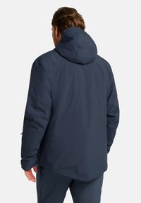 Giacca con cappuccio blu navy, in tessuto morbido, vestibilità rilassata, vista posteriore, con cerniere laterali e cappuccio regolabile, adatta per uso esterno.