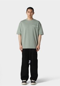 Lysgrønt oversized t-shirt med rund hals, prydet med hvid tekst. Sammen med sort løstsiddende cargo bukser og sorte sneakers.