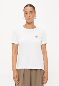 Witte katoenen t-shirt met ronde hals, korte opgerolde mouwen en twee kleine hartpatronen in goud en beige op de linkerborst.
