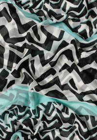 Lightweight scarf featuring a bold zigzag pattern in black, white, and teal. The fabric is sheer and slightly crinkled, creating texture.