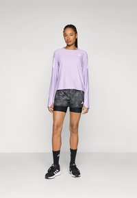 Langermet lavendel treningsgenser, svarte mønstrede shorts, svarte sokker og joggesko. Har Adidas-logo på genseren og shortsene.