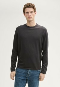Camiseta de manga larga de color gris oscuro, hecha de una tela suave, con un cuello redondo y un corte recto. Se lleva con vaqueros azules.