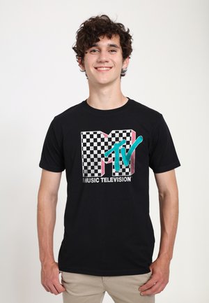 Black cotton t-shirt featuring a checkerboard print and a multicolored 'MTV' logo with glossy accents. Model stands against a plain background.