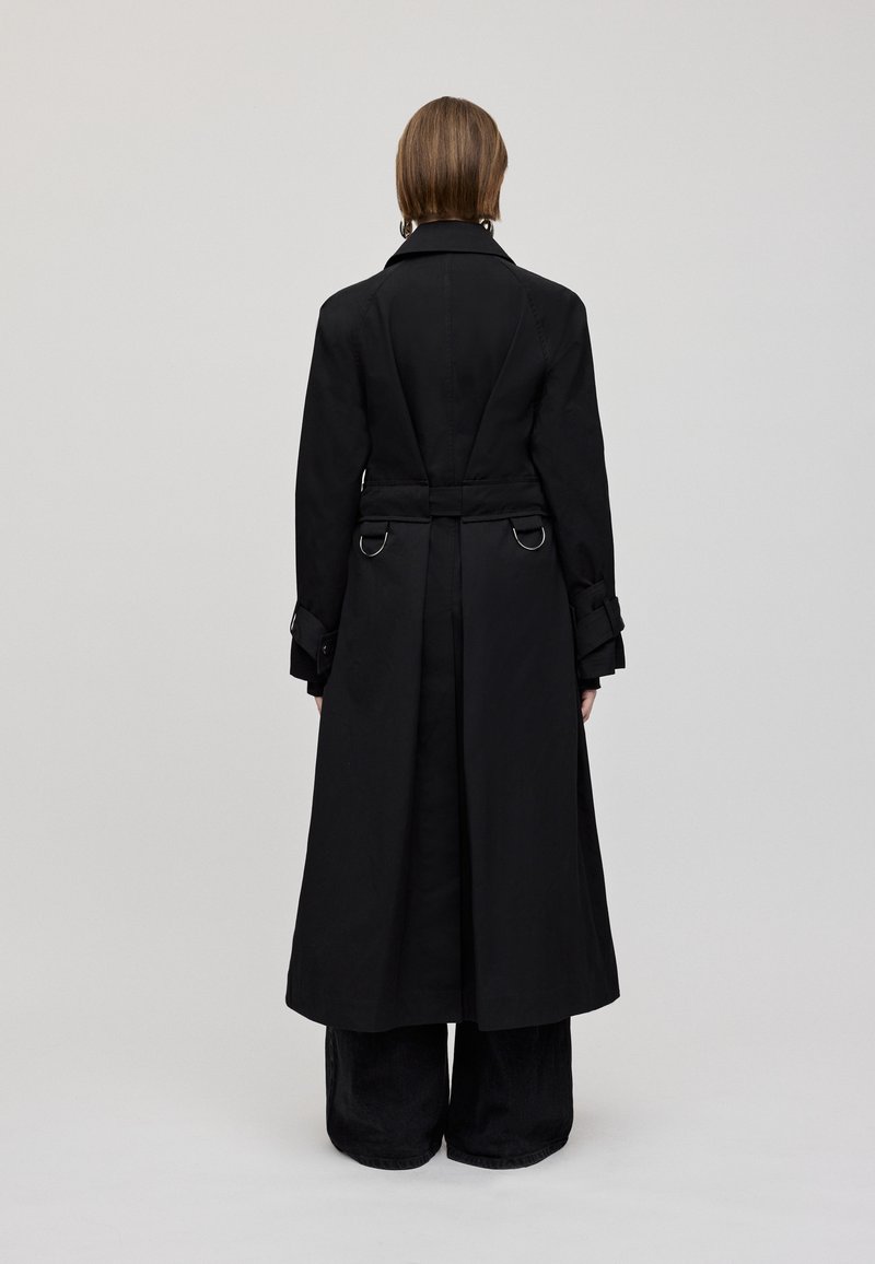Langer schwarzer Mantel aus einem glatten, leichten Material. Verfügt über einen Gürtel, Schlaufenakzente und ein maßgeschneidertes Design. Rückansicht zeigt klare Linien.