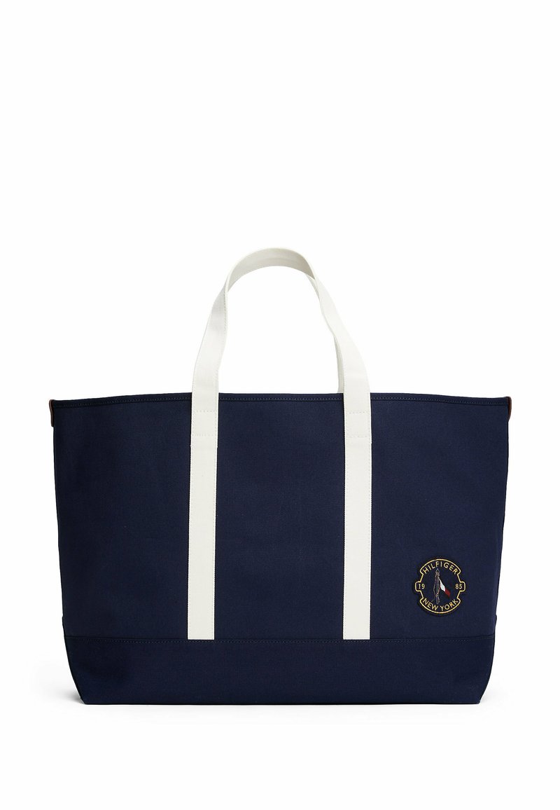 Borsa tote in tela blu navy con manici bianchi, caratterizzata da un dettaglio in rilievo del logo tondo ricamato. Forma rettangolare strutturata con una sottile texture.