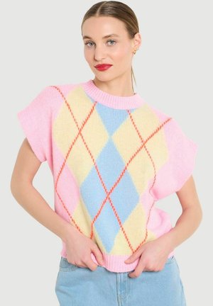 Femme portant un pull rose à manches courtes avec un motif argyle jaune pastel et bleu, assorti à un jean bleu clair, les mains tenant l'ourlet.