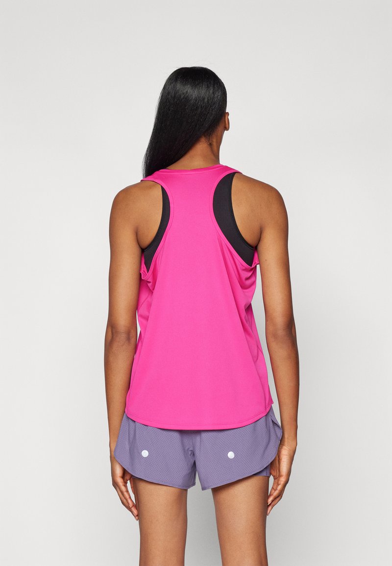 Top sportivo a maniche corte di un vivace rosa antico con armholes neri, abbinato a pantaloni corti larghi viola con accenti bianchi e una trama testurizzata.