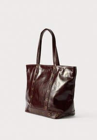 Bordowa skórzana torba na ramię z błyszczącym wykończeniem, z złotymi oczkami wzdłuż szwów oraz solidnymi uchwytami dla łatwego noszenia.