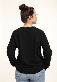 Felpa nera a maniche lunghe realizzata in tessuto morbido, con scollo rotondo, vestibilità rilassata e polsini a coste, abbinata a jeans azzurri chiari.