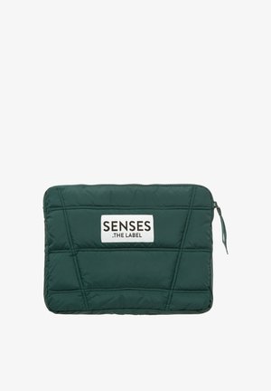 Green quilted laptop sleeve with a white label reading "SENSES .THE LABEL," featuring a zip closure and geometric stitching details.