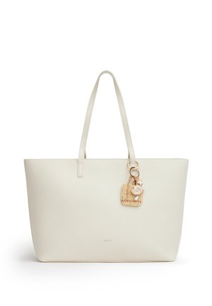 Borsa tote color crema con due spallacci e un piccolo charm intrecciato con conchiglie e perline attaccato a uno spallaccio.