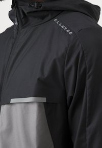 Svart och grå jacka med dragkedja fram, huva och ett stort bröstfack. Har en elegant design med en jämn textur och diskret logodetalj.