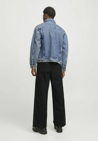 Denimjakke i mellemblå, med spidse kraver, lange ærmer og en afslappet pasform. Båret med sorte bred ben bukser og sorte støvler.
