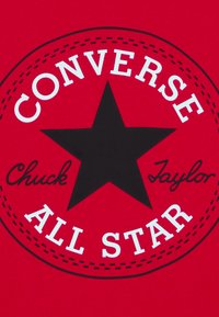 Conception graphique rouge avec une étoile noire portant les inscriptions « CONVERSE » et « ALL STAR » en texte blanc, et « Chuck Taylor » en style cursif en dessous.