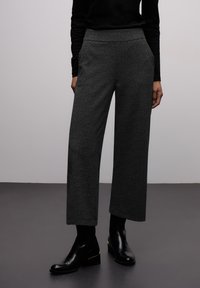 Pantalon gris à jambes larges avec tissu texturé et poches latérales, associé à des bottines noires et un haut noir à manches longues.