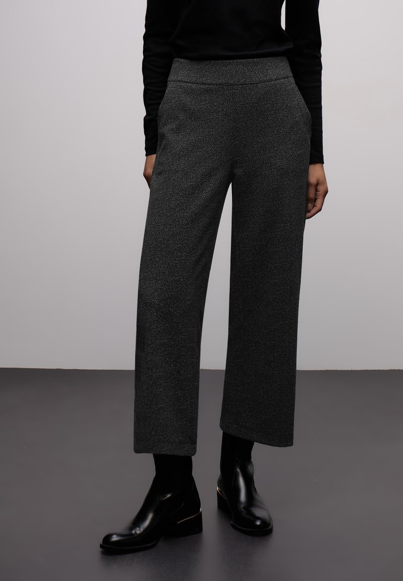 Pantalon gris à jambes larges avec tissu texturé et poches latérales, associé à des bottines noires et un haut noir à manches longues.