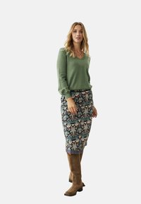 Suéter de punto verde con mangas largas y escote en V, combinado con una falda lápiz estampada que presenta diseños florales en tonos azules y rosas, y botas marrones.