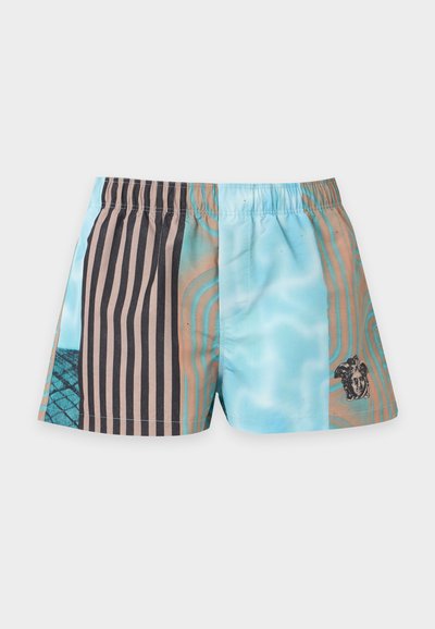 Short de bain pour homme à taille élastique, orné de rayures verticales noires et de motifs ondulés bleus, avec un petit motif de tête de Méduse sur une jambe.