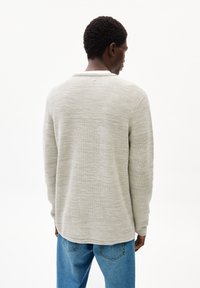 Hellgrau gestrickter Pullover mit strukturiertem Muster, runder Ausschnitt und langen Ärmeln, kombiniert mit blauen, lässig geschnittenen Jeans.