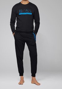 Felpa nera a maniche lunghe e pantaloni abbinati. Presenta il logo blu "BOSS" sul petto e sul lato. Tessuto morbido con polsini e cintura a coste.