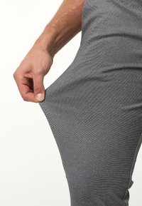 Pantalones deportivos grises con tela texturizada, material elástico y una mano agarrando el costado para una vista más cercana del diseño.
