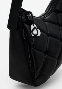 Black quilted leather handbag with rounded shape, featuring a zip closure and a heart-shaped metal tag with a logo. Smooth texture.
